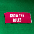 A piece of pink fabric with the words 'know the rules' written on it against a green background