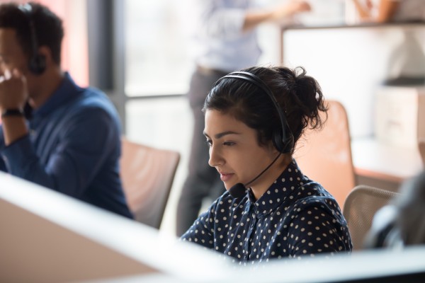 A woman sitting at desk wearing a headset, answering a phone call