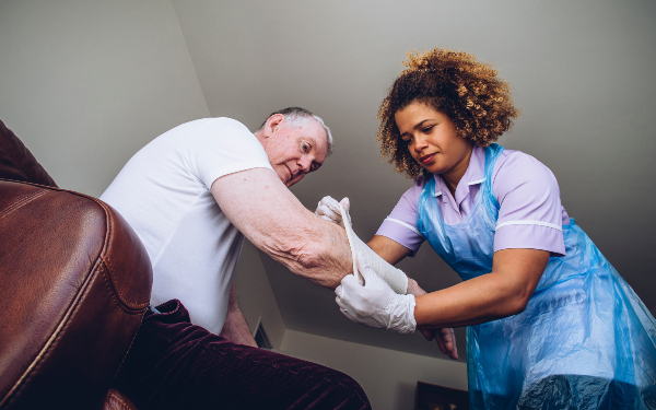 Care worker putting a bandage on a man's arm in his home.