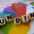 The word 'funding' spelt out in blocks against the background of some graphs