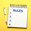 Notebook with list of rules and pen on yellow background, flat lay