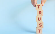 Person building tower of blocks spelling out 'trust'