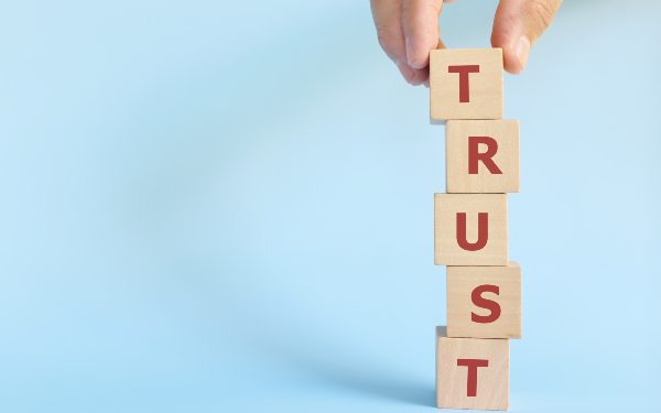 Person building tower of blocks spelling out 'trust'