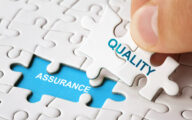 Person putting jigsaw piece with word 'quality' written on it on to space with 'assurance' written on it