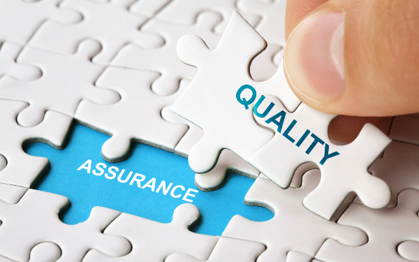 Person putting jigsaw piece with word 'quality' written on it on to space with 'assurance' written on it