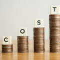 Piles of coins of increasing size with tiles spelling out the word 'cost' sitting on each