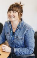 Rachael wearing a denim jacket and smiling away from the camera. She has brown hair