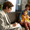 Social worker making notes in document while talking to mother and child on a sofa