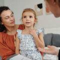 Mother looking at young daughter, who is sitting on her lap, during session with a social worker