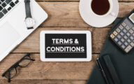 Terms and Conditions text, Office desk with electronic devices, computer and paper, wood table from above, concept image for blog title or header image.