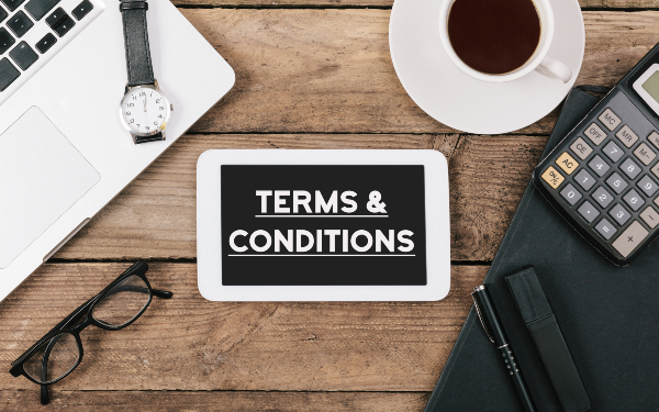 Terms and Conditions text, Office desk with electronic devices, computer and paper, wood table from above, concept image for blog title or header image.