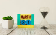 Image of march 31 on a wooden coloured calendar, next to sandtimer on white background