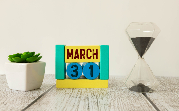 Image of march 31 on a wooden coloured calendar, next to sandtimer on white background