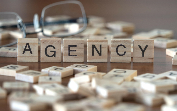 agency word or concept represented by wooden letter tiles on a wooden table with glasses and a book