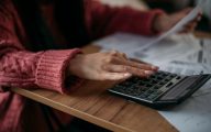 Close-up of woman's hands with calculator and utility bills. The concept of rising prices for heating, gas, electricity. A lot of utility bills and hands in a warm sweater on a calculator