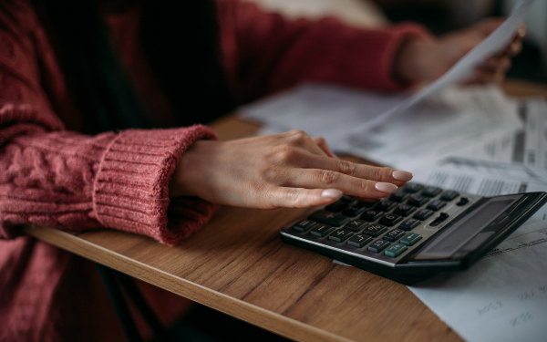 Close-up of woman's hands with calculator and utility bills. The concept of rising prices for heating, gas, electricity. A lot of utility bills and hands in a warm sweater on a calculator