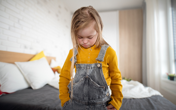 A sad little girl with Down syndrome looking down at home.