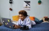 Young man lying on bed looking at his laptop