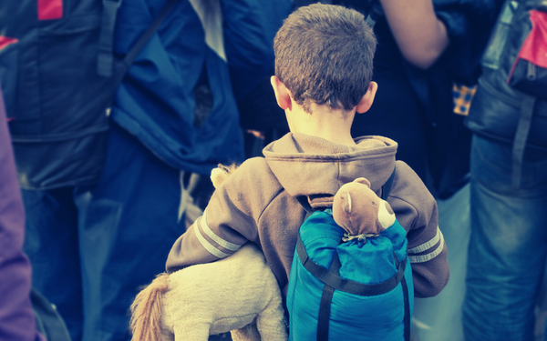 A young boy walking in a group with a small rucksack on his back, to symbolise asylum seeking