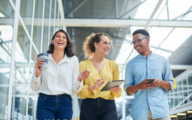 Walking, conversation and business people in office laughing, bonding and talking on lunch break. Happy, friends and group of creative directors with coffee, tablet and phone in workplace together