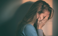 A blonde female covering her face with her hands.