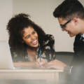 Two colleagues, one woman and one man, working together over a laptop and laughing.