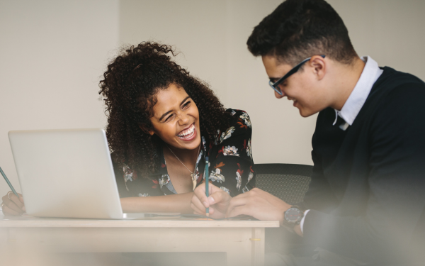 Two colleagues, one woman and one man, working together over a laptop and laughing.